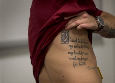 This photo taken May 13, 2014 shows medically retired Marine Lance Cpl. Kyle Carpenter lifting his shirt to show a tattoo on his side as he speaks with media at the Pentagon. The tattoo reads "Blessed be the Lord my rock, who trains my hands for war, and my fingers for battle. The White House announced Monday that Carpenter, 24, will receive the medal of honor on June 19. He is the 15th recipient of the medal for service in Iraq and Afghanistan, the eighth still alive. (AP Photo/Carolyn Kaster)