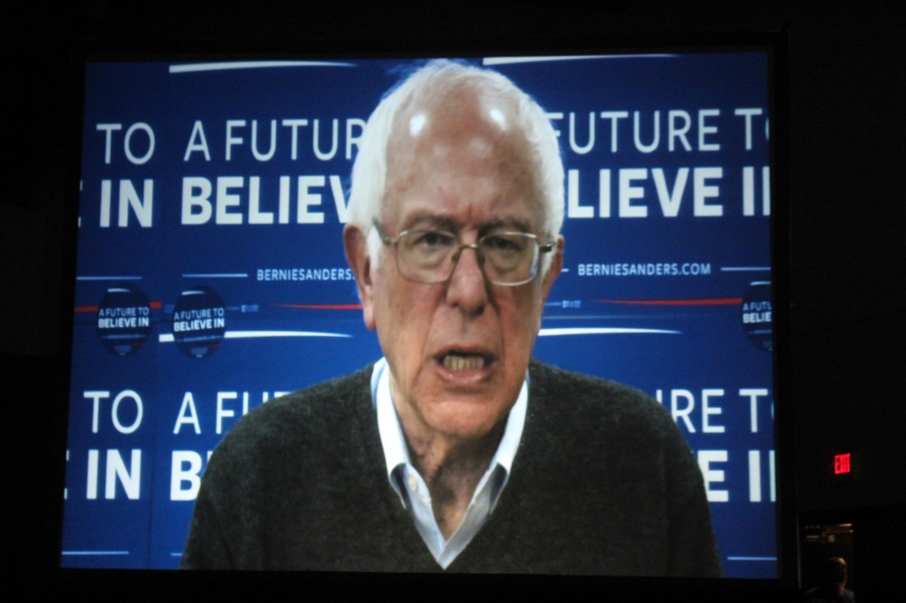 Presidential candidate Bernie Sanders delivers videotaped message on  screen.