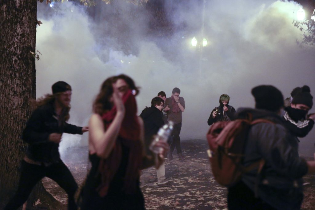 Police in downtown Portland, Ore., attempt to disperse people protesting the election of President-elect, Donald Trump, Friday, Nov. 11, 2016. In Portland, police used tear gas and flash-bang grenades Friday to try to disperse the crowd after hundreds of people marched through the city, disrupting traffic and spray-painting graffiti. Authorities said "burning projectiles" were thrown at police and vandalism and assault had taken place during the rally, which organizers had billed as peaceful earlier in the day.  (Stephanie Yao Long/The Oregonian via AP)