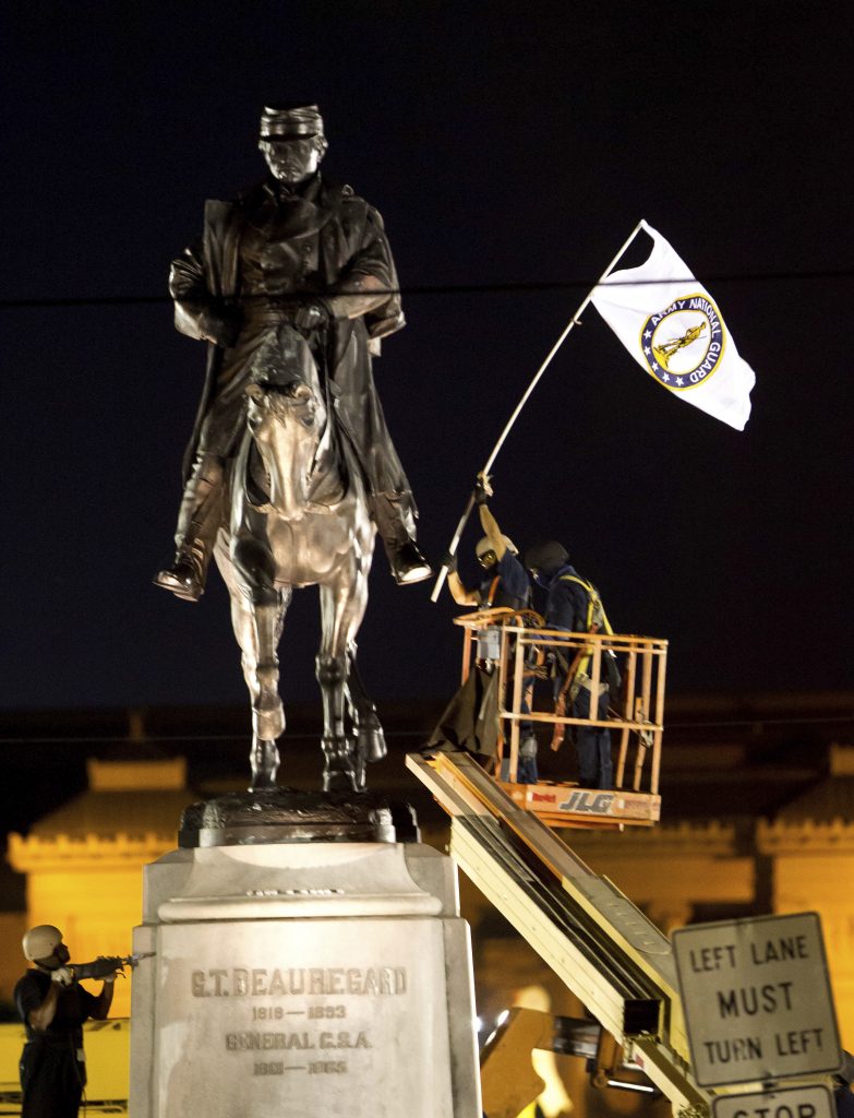 A worker in protective gear takes down an Army National Guard flag from the statue of Confederate General P.G.T. Beauregard during the statue's removal from the entrance to City Park in New Orleans, Tuesday, May 16, 2017. The city announced late Tuesday that it had begun the process of removing a statue of Confederate Gen. P.G.T. Beauregard — the third of four monuments city officials plan to take down across the city.  (AP Photo/Scott Threlkeld)